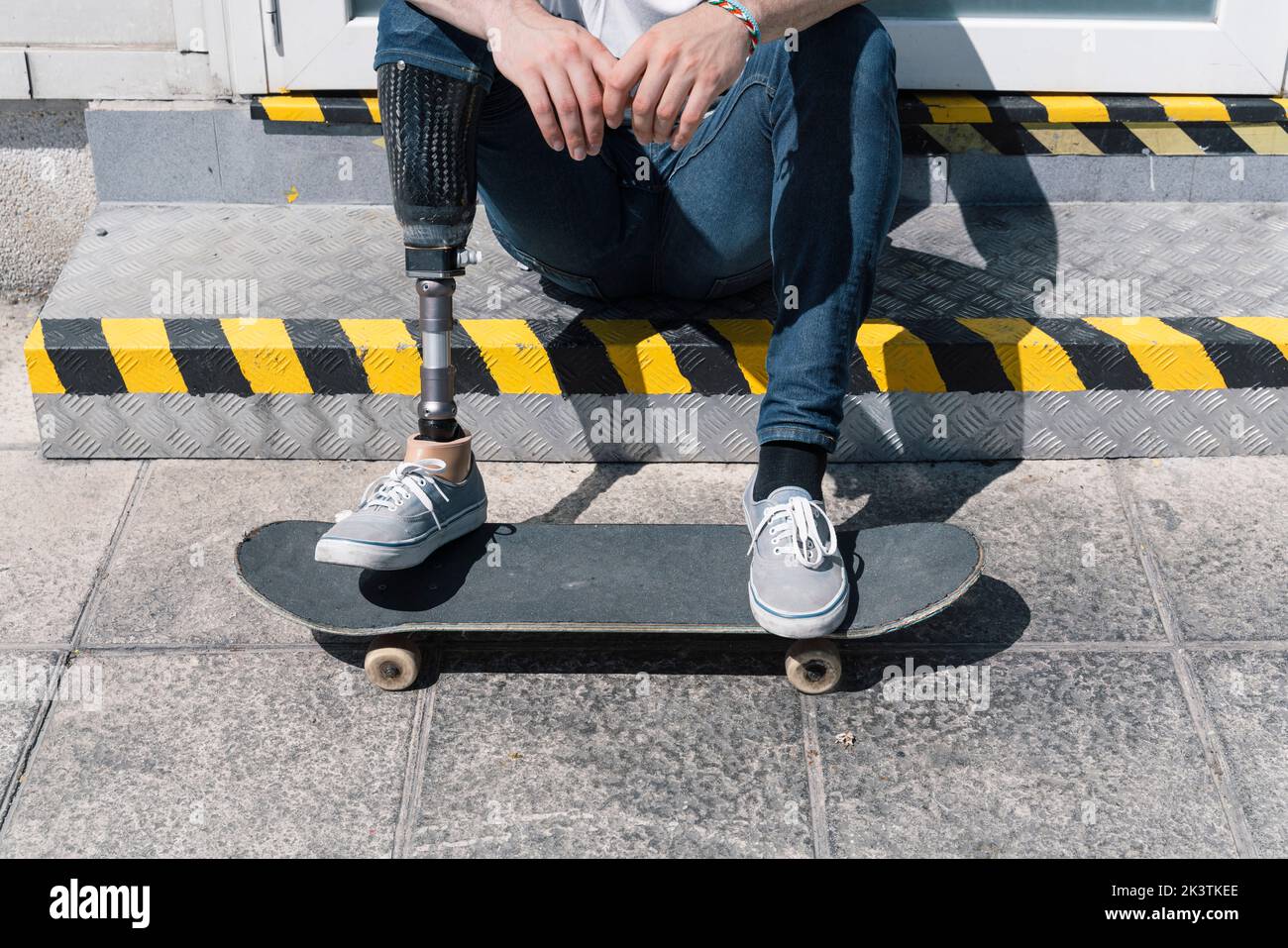 From above anonymous male with artificial leg sitting on step near skateboard on sunny day on city street Stock Photo