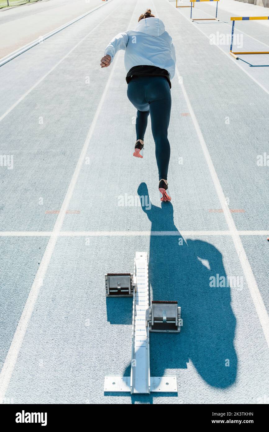 Back view of unrecognizable sportswoman beginning to run fast from
