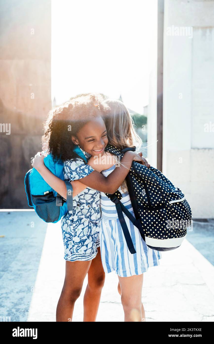 Laughing African American girl embracing friend standing on street in bright day Stock Photo