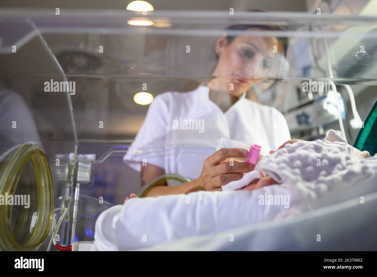 Medical worker feeding premature baby with tubes attached in modern