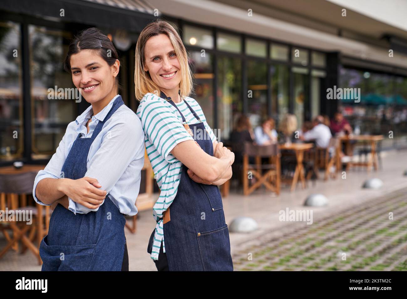 Photo of two happy female restaurant owners standing back to back in front of their restaurant Stock Photo