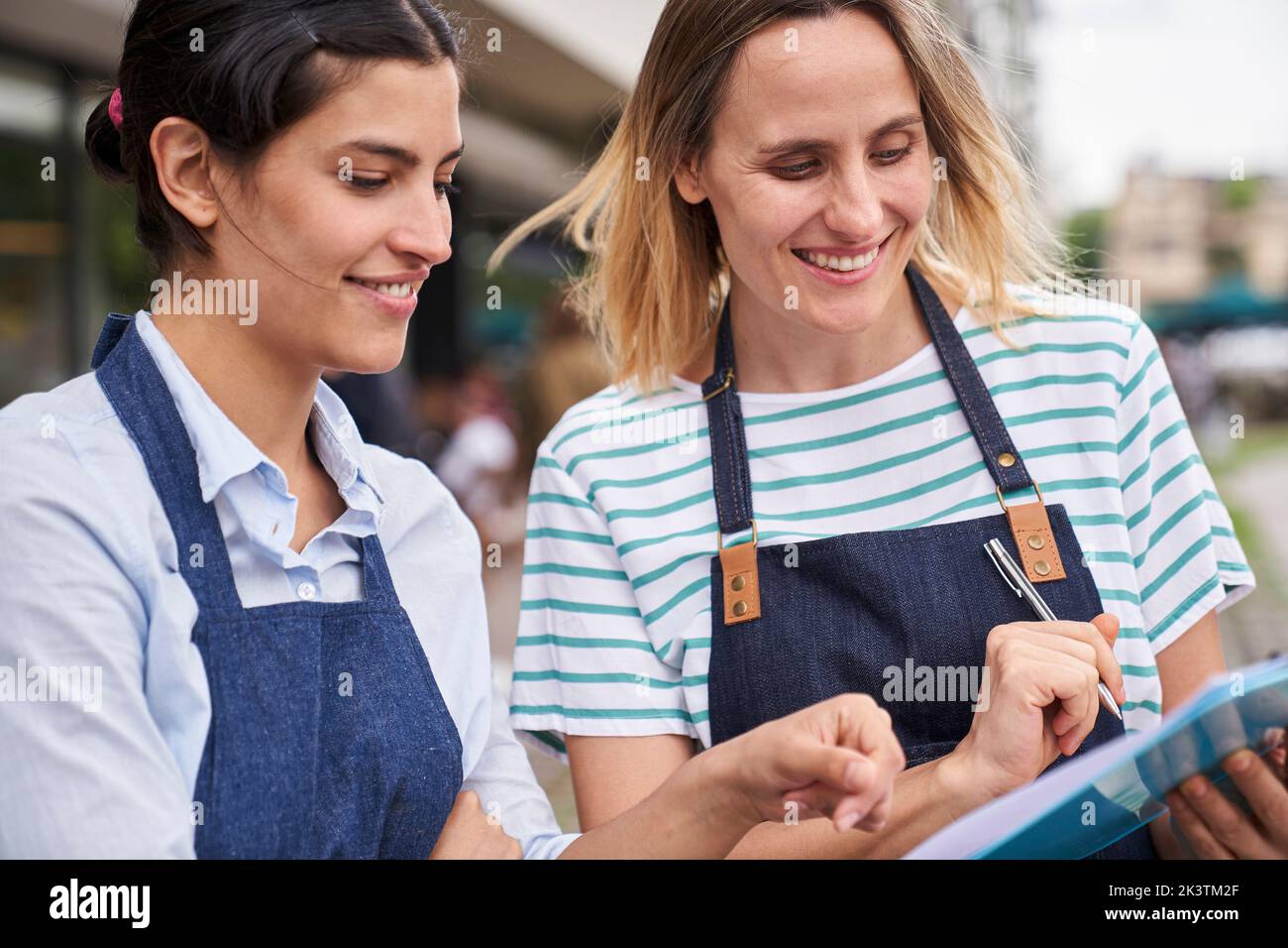 Two successful female entrepreneurs checking a list in front of their restaurant Stock Photo