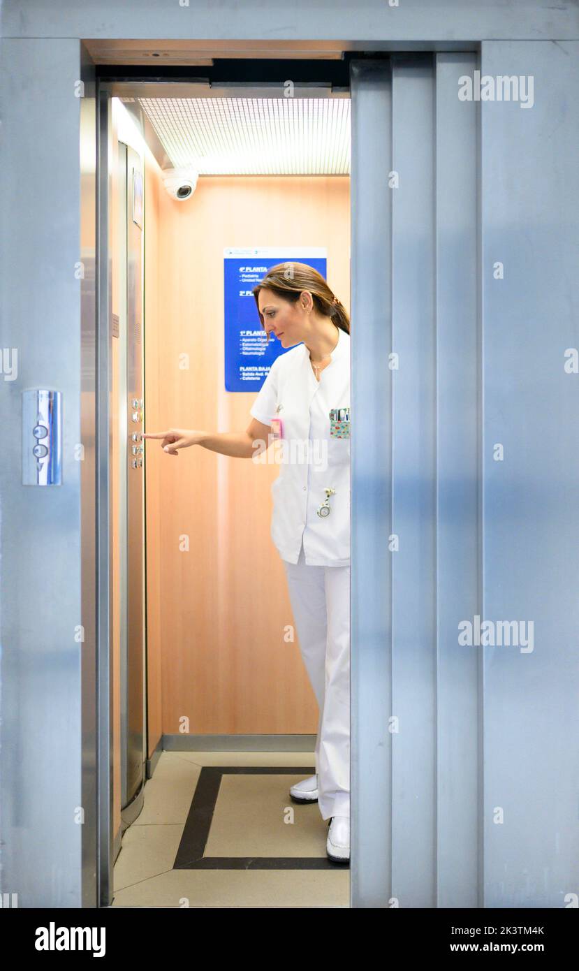 Full body woman in white medical uniform pushing button inside elevator while working in hospital Stock Photo