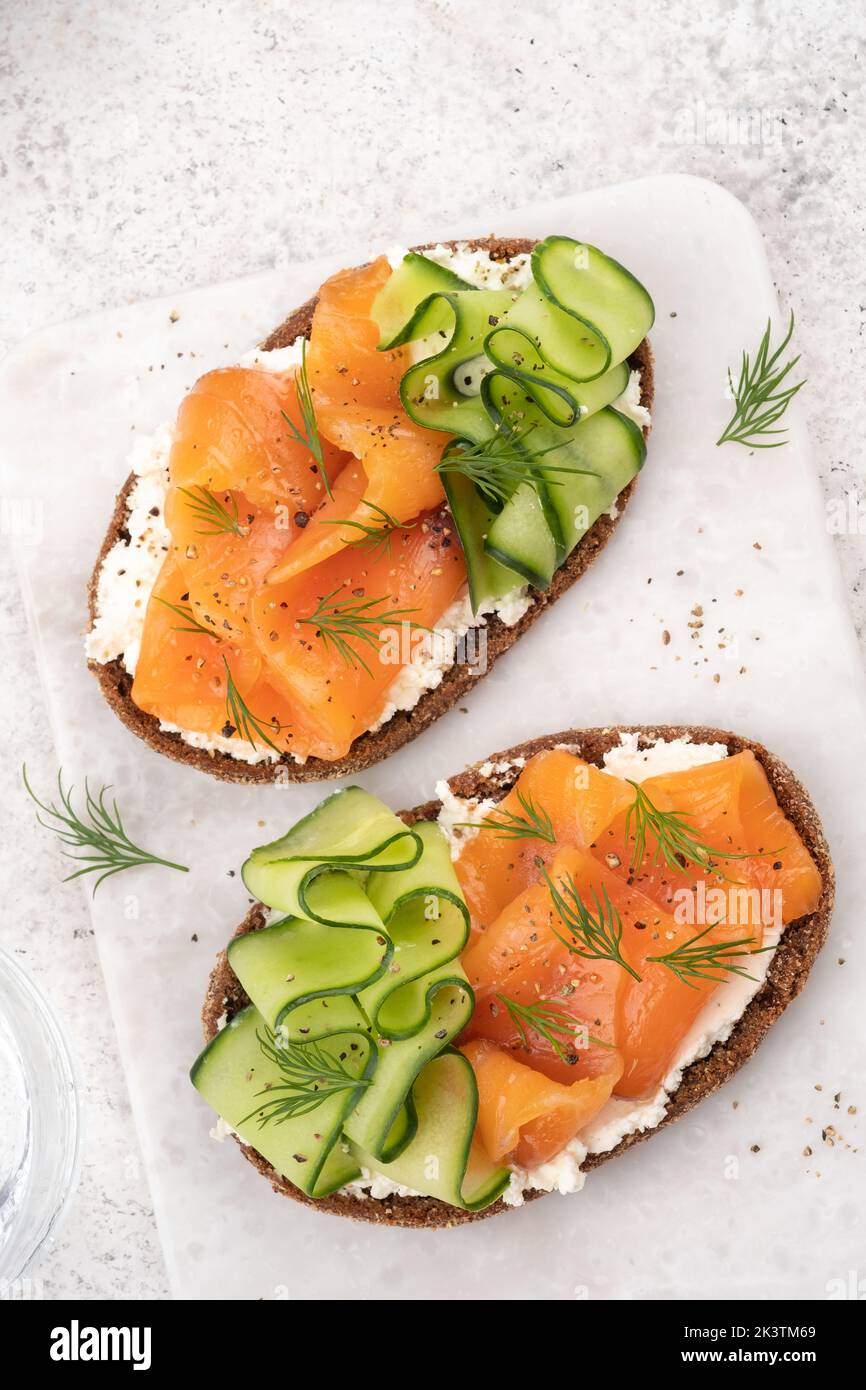 Rye bread open sandwiches with salted salmon and cucumber on a white stone table. Healthy food. Stock Photo