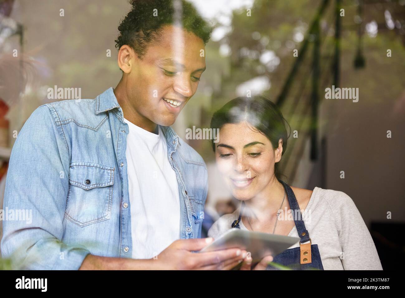 Small business owners standing behind window while using digital tablet Stock Photo