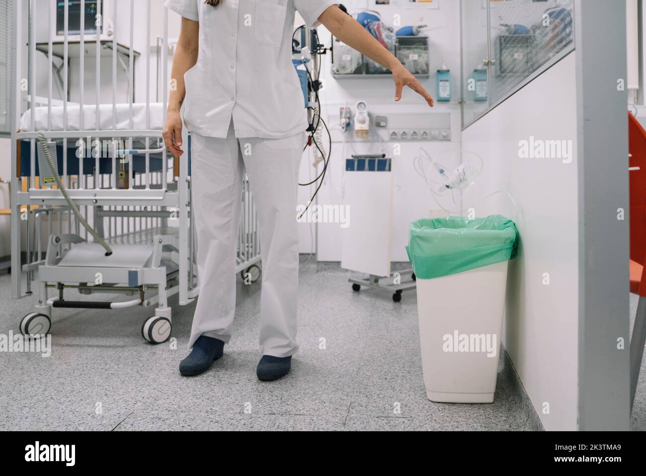 Crop faceless doctor in white uniform throwing medical waste in bucket