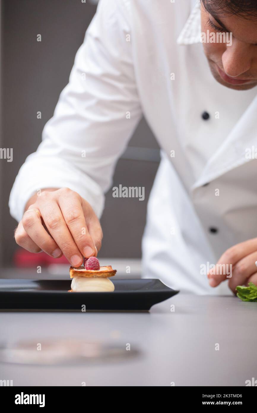 Crop focused man in white chef jacket decorating fancy dish with raspberry on plate Stock Photo