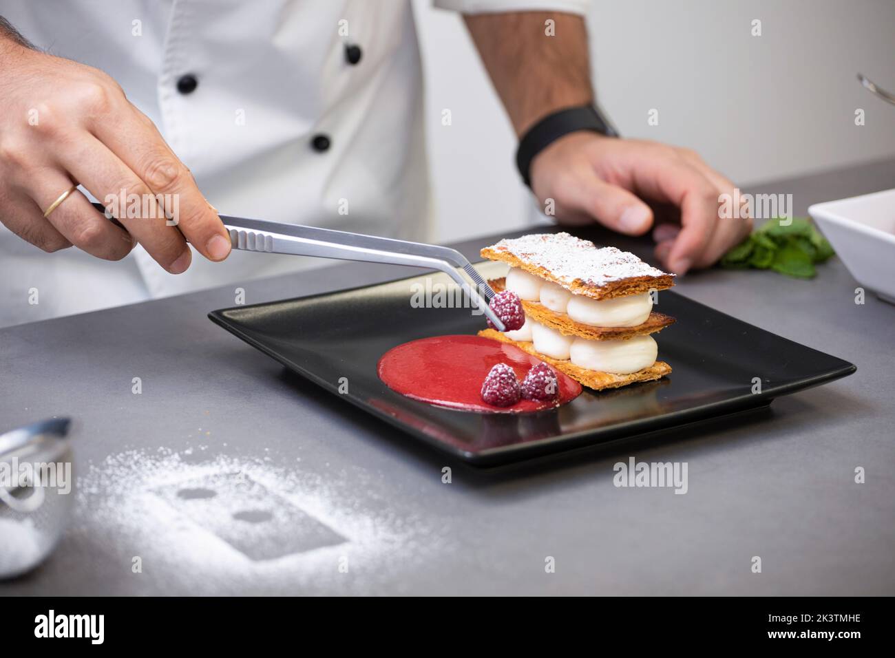 Crop focused man in white chef jacket decorating fancy dish with raspberry on plate Stock Photo