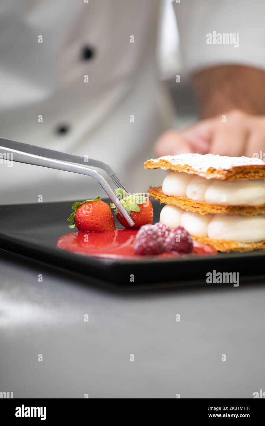 Crop focused man in white chef jacket decorating fancy dish with raspberry on plate Stock Photo