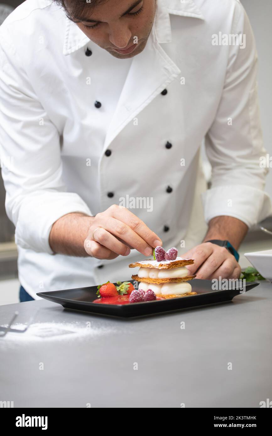 Crop focused man in white chef jacket decorating fancy dish with raspberry on plate Stock Photo