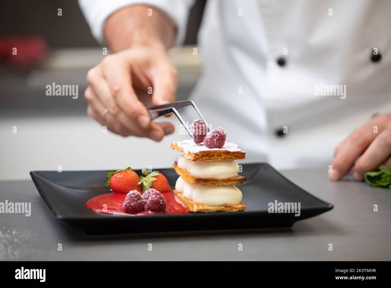 Crop focused man in white chef jacket decorating fancy dish with raspberry on plate Stock Photo