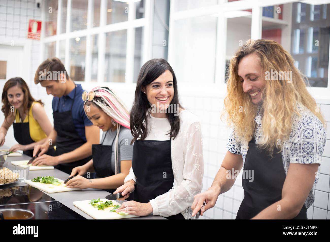 Side view of attentive multi ethnic people slicing vegetables with knife while standing together in kitchen with professional equipment Stock Photo
