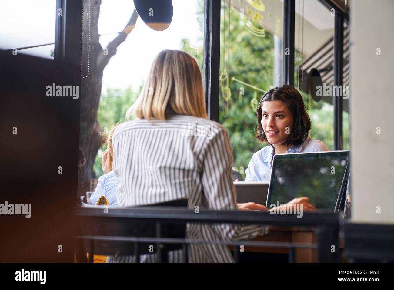 Mid-shot of two female entrepreneurs discussing business while working at cafe Stock Photo