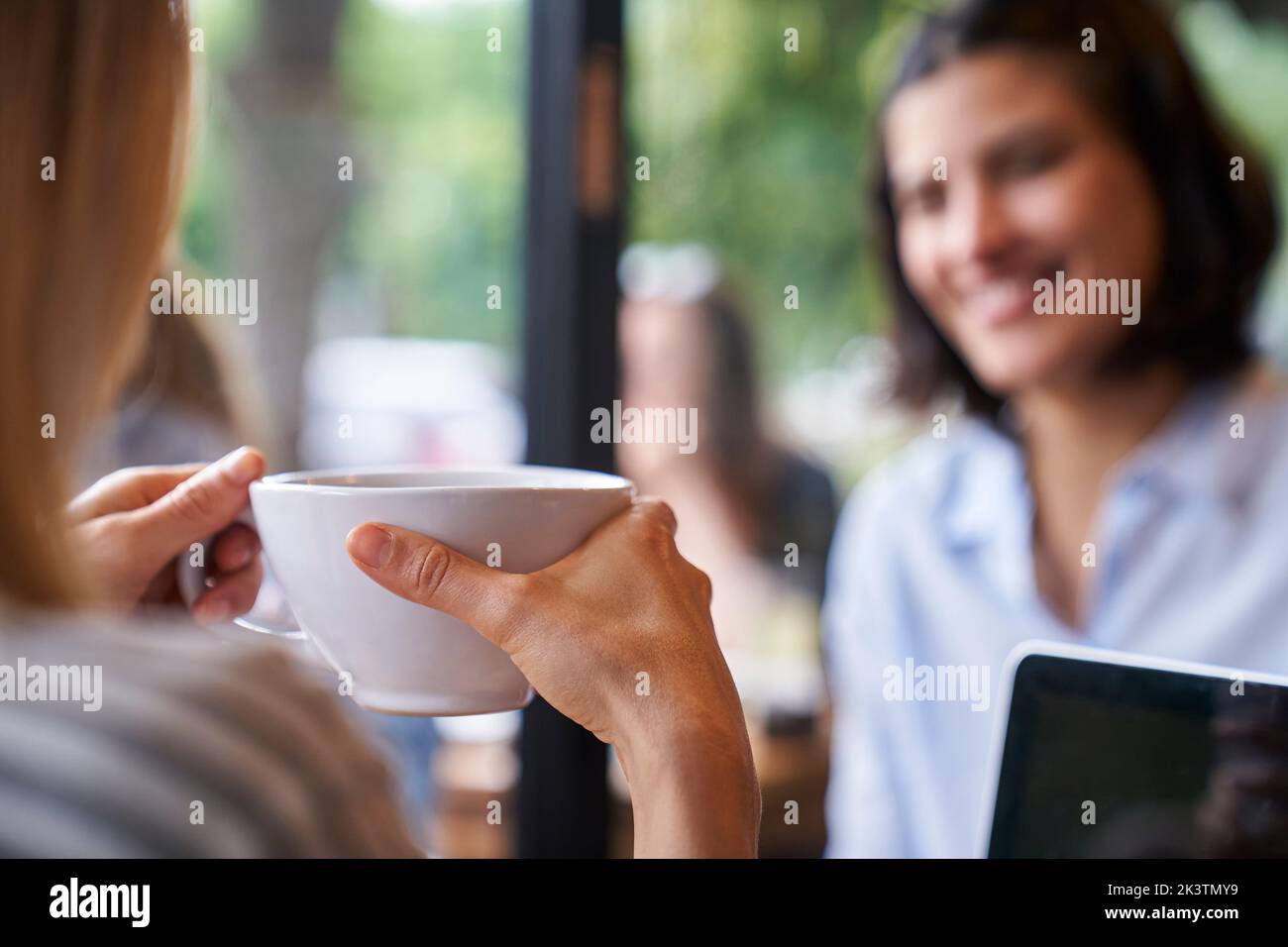 Close-up shot from behind of woman holding a cup of coffee and talking to a friend Stock Photo