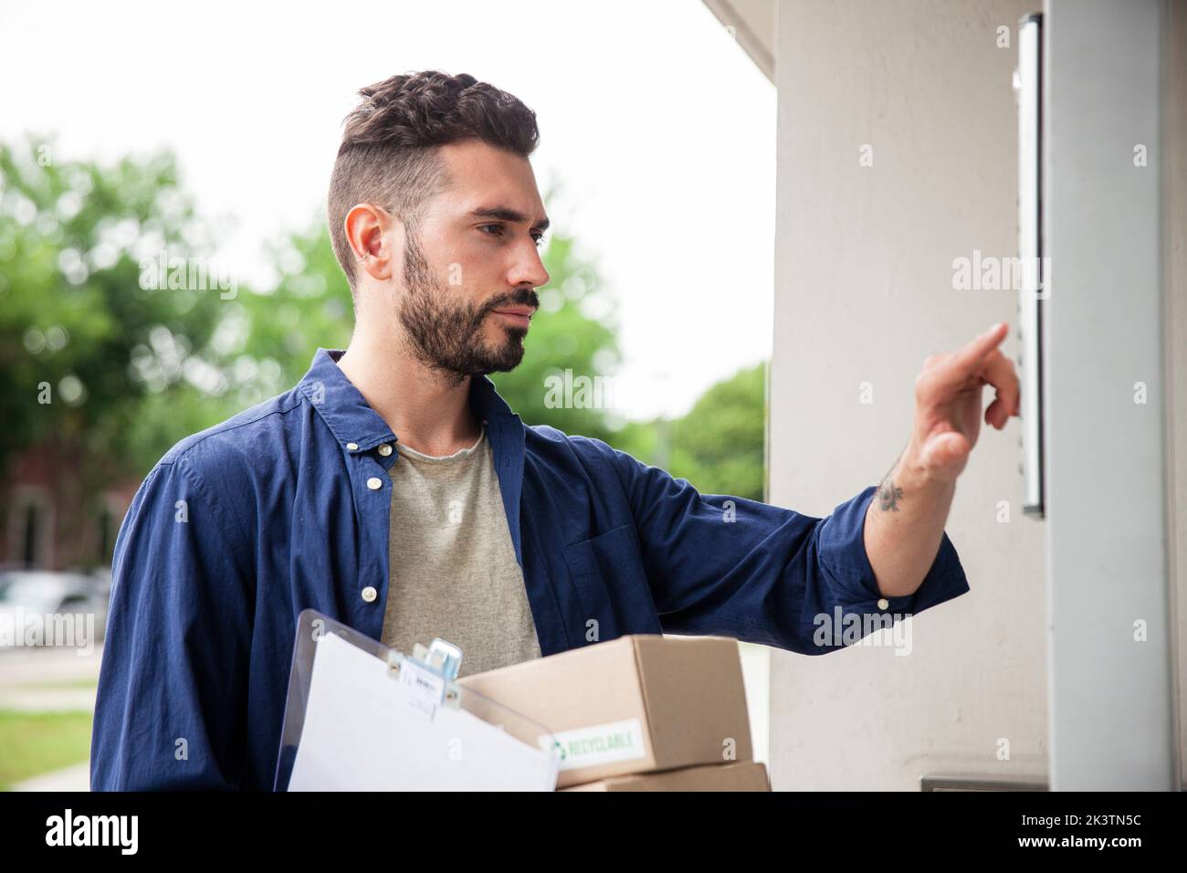 Delivery man standing in front of doorway while ringing doorbell Stock Photo