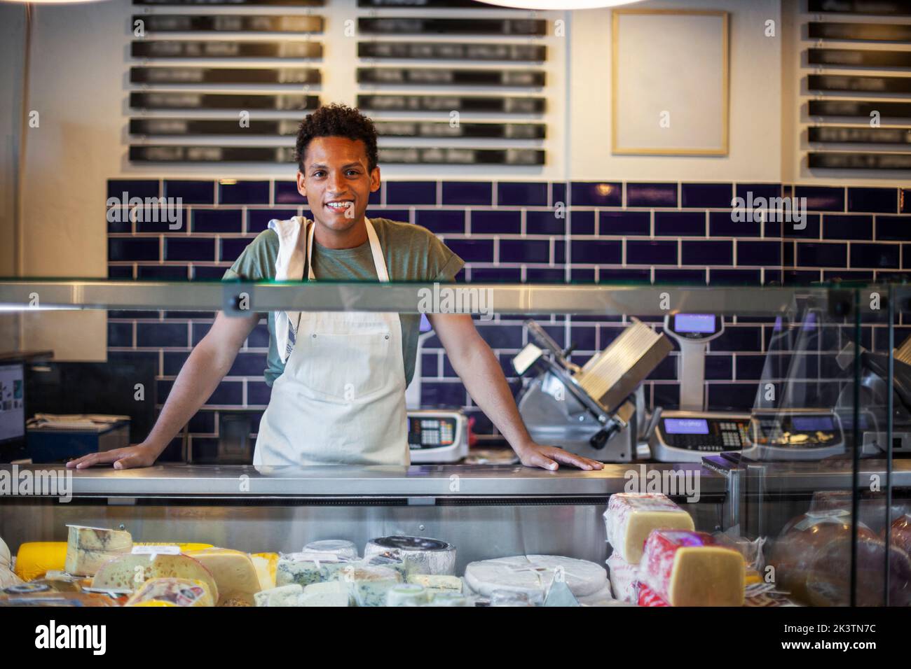 Smiling Latin American young man standing behind counter in cheese