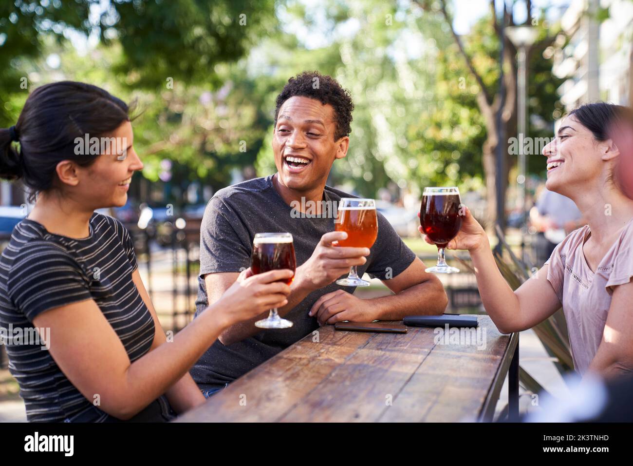 Mid-shot photo three young diverse friends raising their beers to make a toast at happy hour Stock Photo