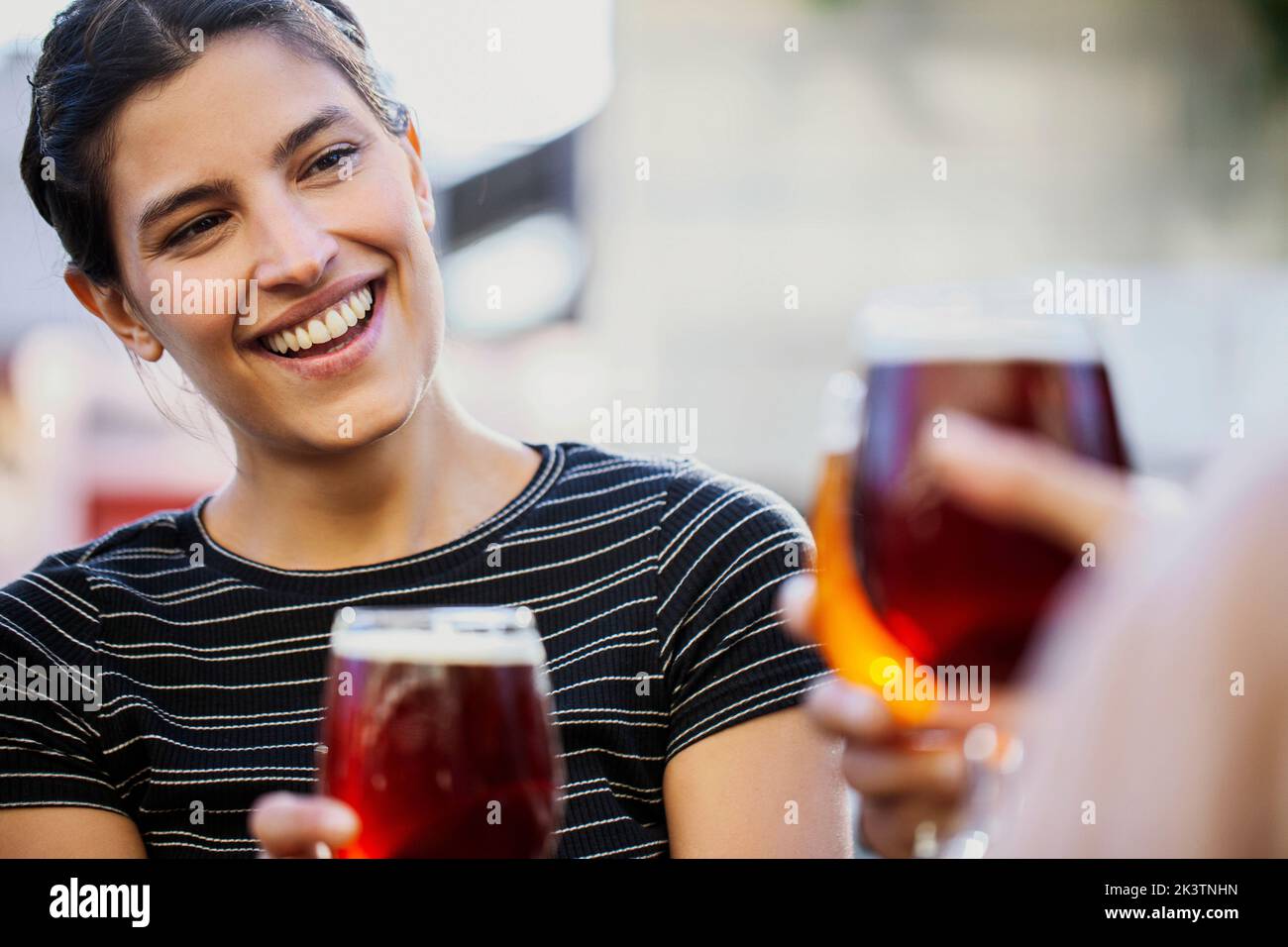 Smiling young adult woman toasting beer cups with friends Stock Photo