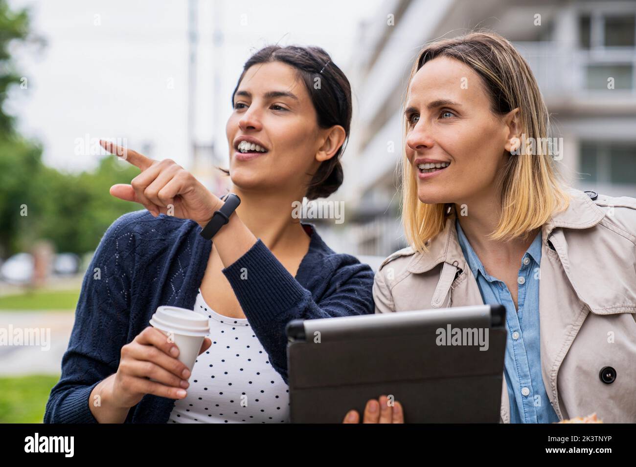 Mid-shot of two female freelance workers doing business and pointing at something while working outdoors Stock Photo