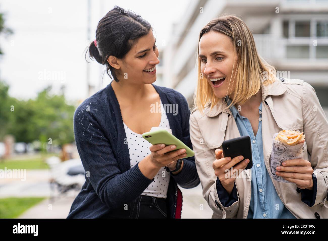 Mid-shot front view photo of two female digital nomads sharing their postings online with their smartphones Stock Photo