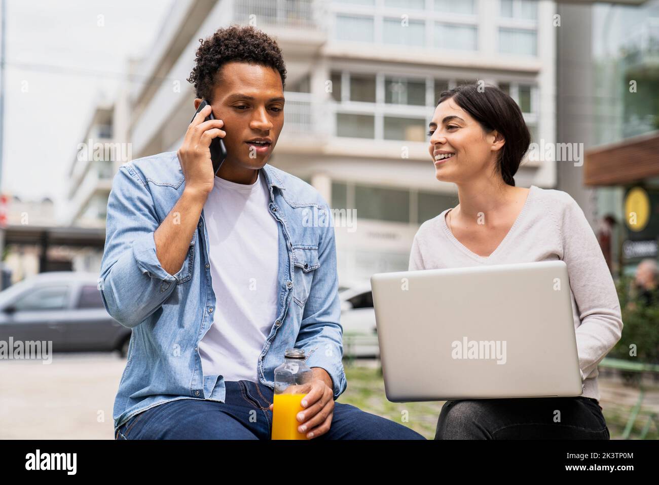 Mid-shot of diverse couple of co-workers discussing business matters while working outdoors Stock Photo