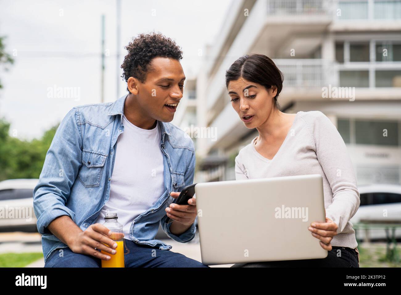 Mid-shot of African-American man and Latin American woman using laptop while working outdoors Stock Photo