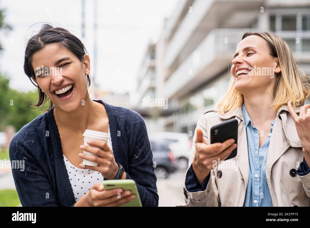 Medium shot of two female entrepreneurs laughing and enjoying content found on social media while working outdoors Stock Photo