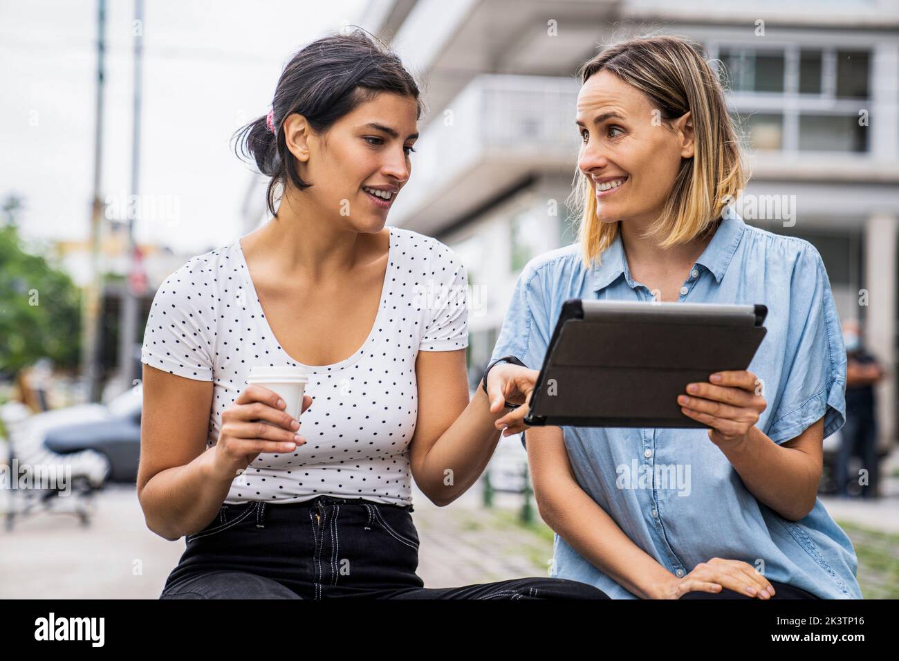 Front view mid-shot of two female co-workers talking about work matters while working outdoors Stock Photo