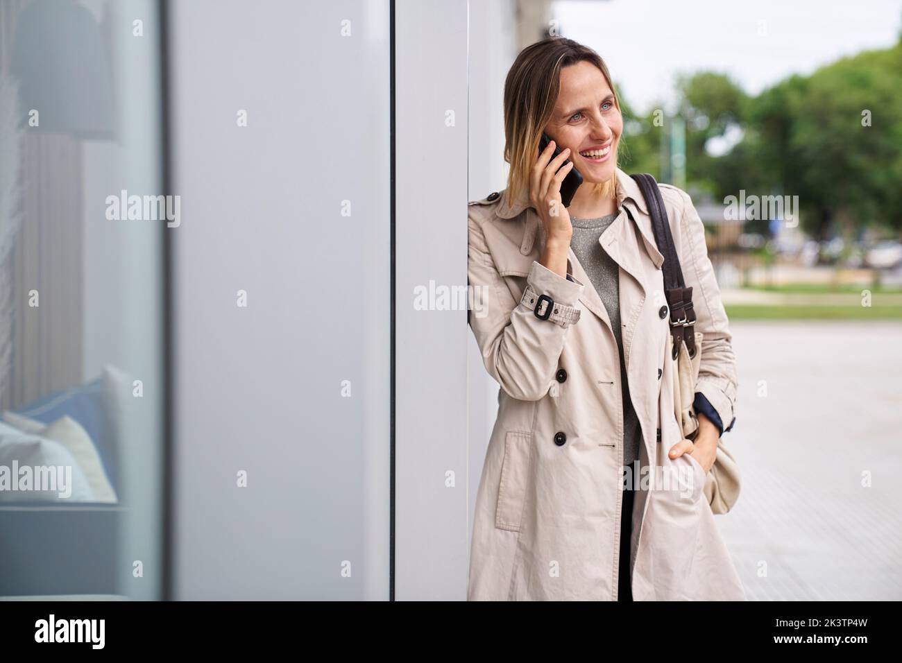 Photo of smiling woman with raincoat speaking on mobile phone in the street Stock Photo