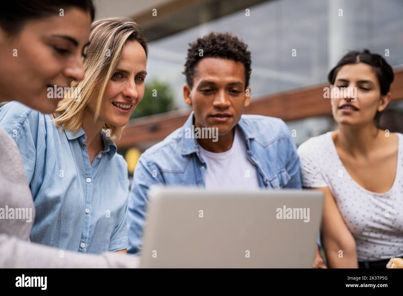 Diverse group of freelance contractor looking at a laptop's screen in an outdoors setting Stock Photo