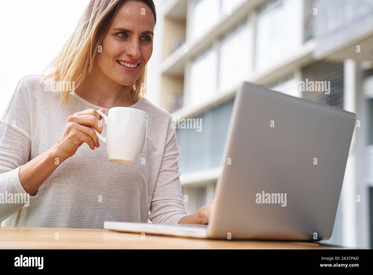 Low angle view of female entrpreneur looking at laptop screen and drinking coffee Stock Photo