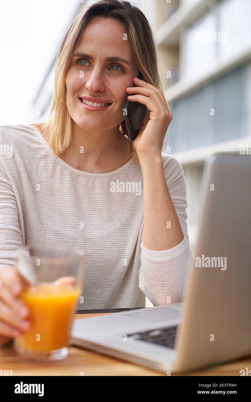 Front view medium shot of woman drinking orange juice in front of laptop computer and speaking