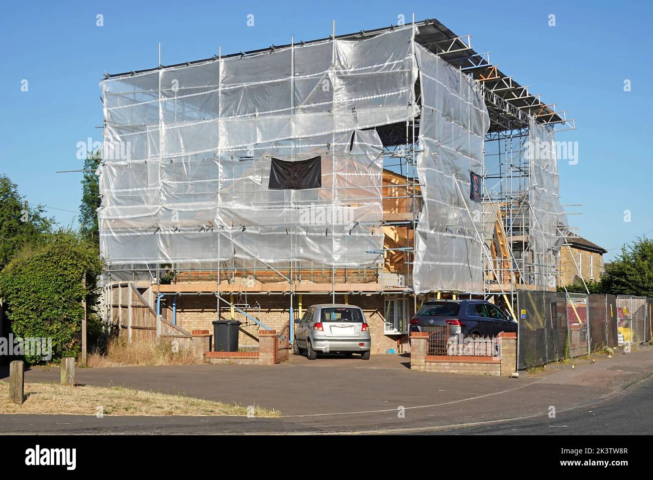 Building construction corner site bungalow conversion to house enclosed in translucent plastic cocoon & corrugated roof on scaffolding framework UK Stock Photo