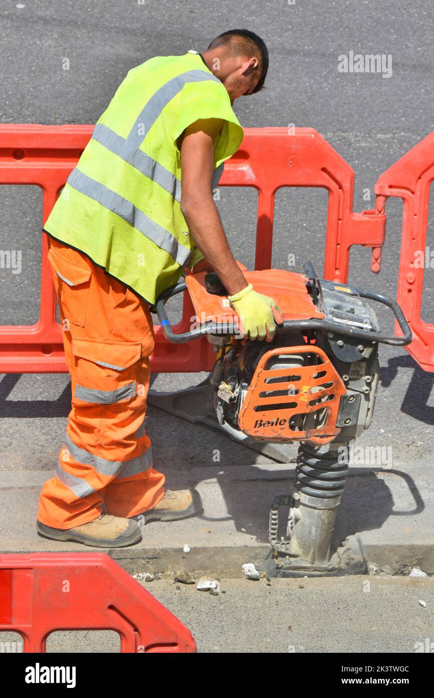 Close up male worker high visibility clothes & diesel engine whacker vibrating compactor tool pavement road works broadband cable trench backfill UK Stock Photo