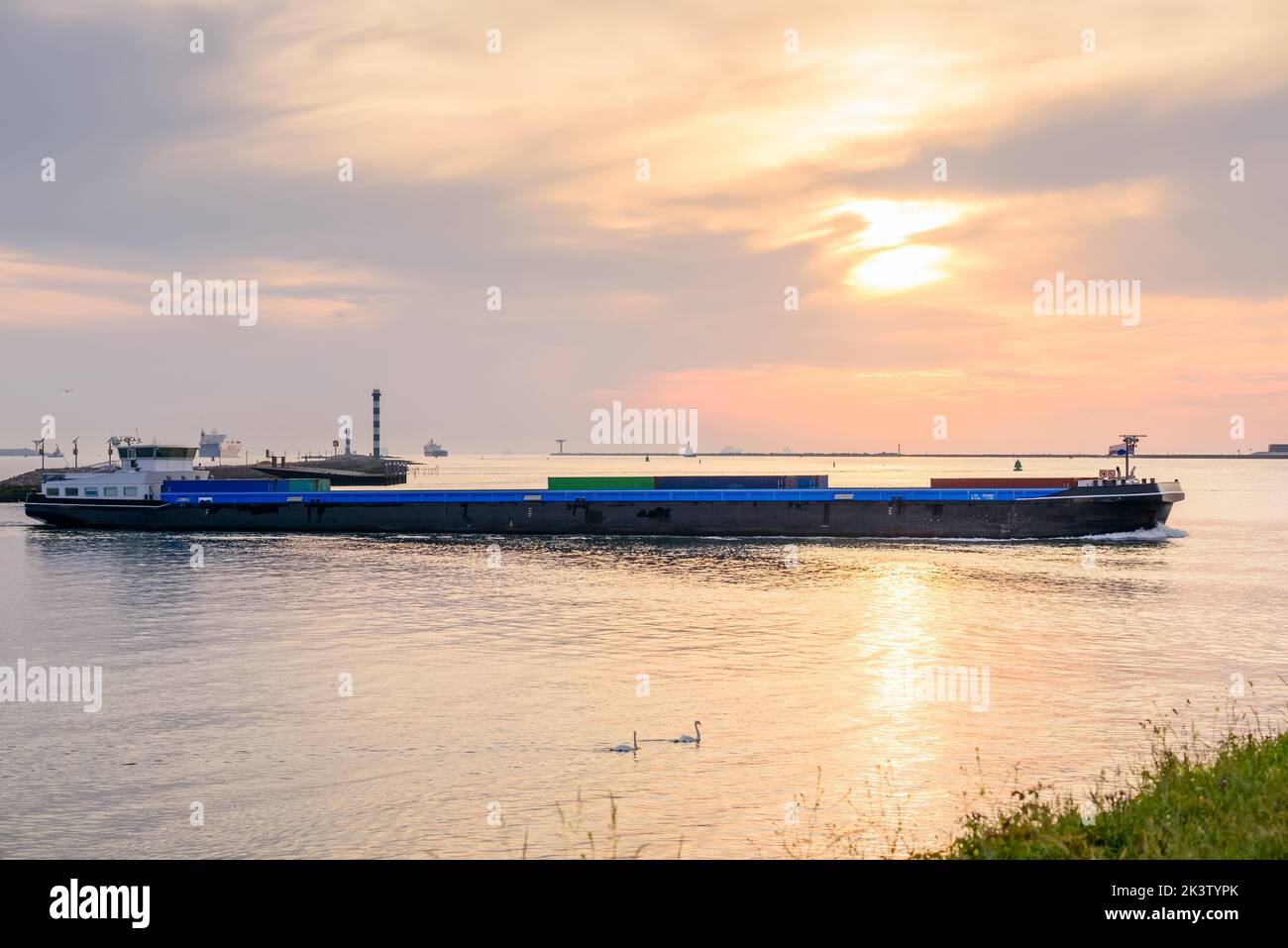 Cargo barge sailing into a harbour at sunset Stock Photo