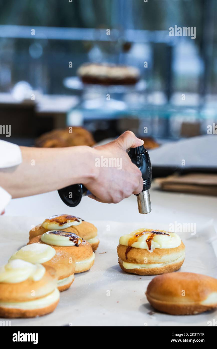 Unrecognizable crop chef caramelizing sugar cream on sweet Berliners ...