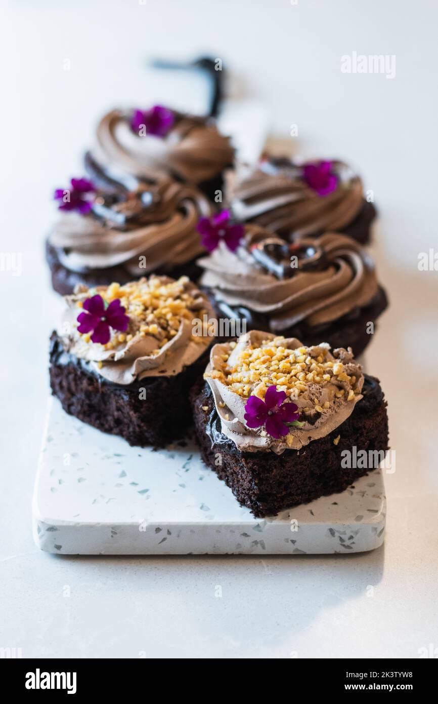 High angle of vegan chocolate sponge cakes with whipped cream and flower decorations served on cutting board on table in bakery Stock Photo