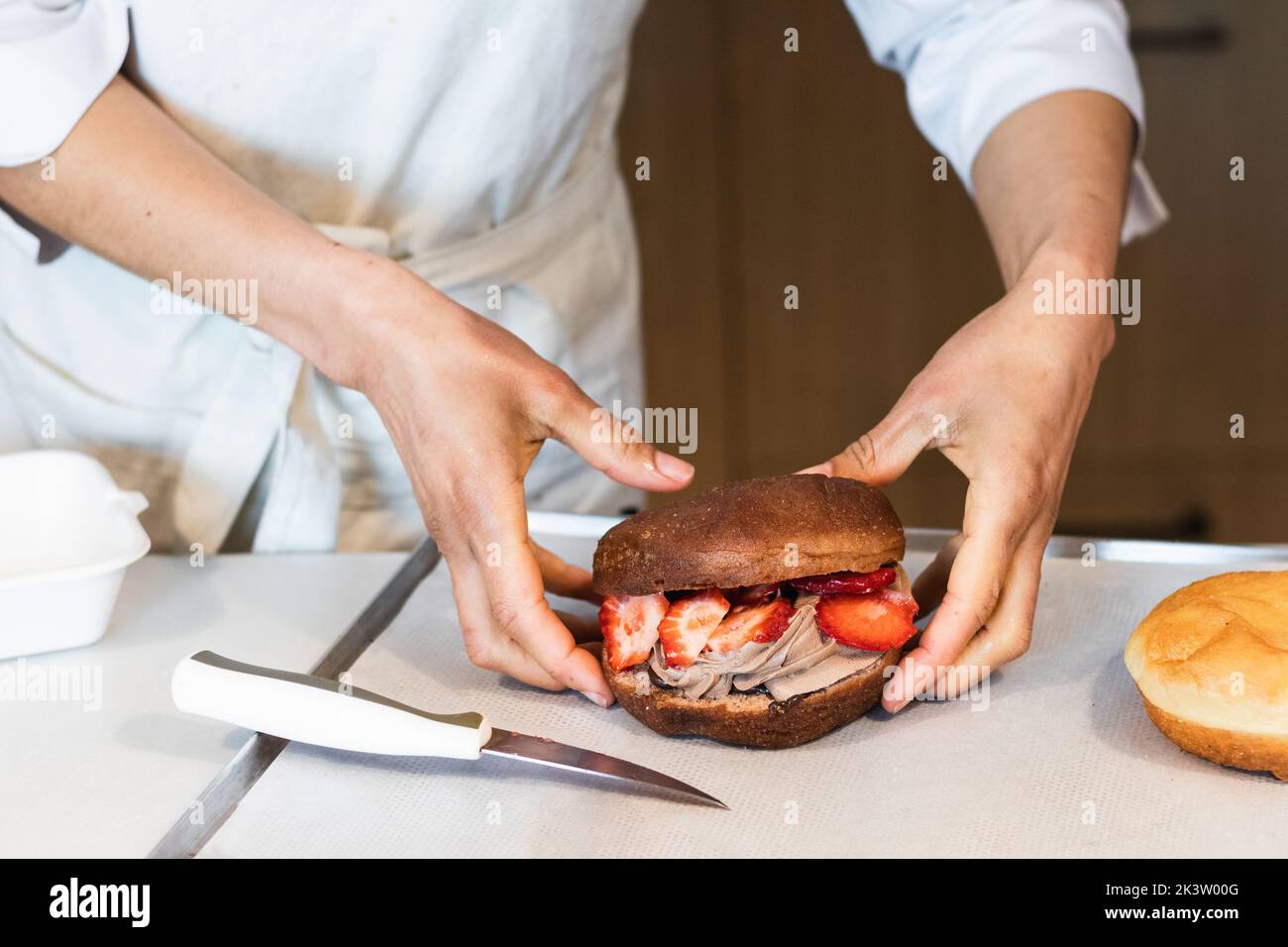 Crop unrecognizable baker holding sweet vegan sponge cake with whipped cream and strawberries in bakery Stock Photo