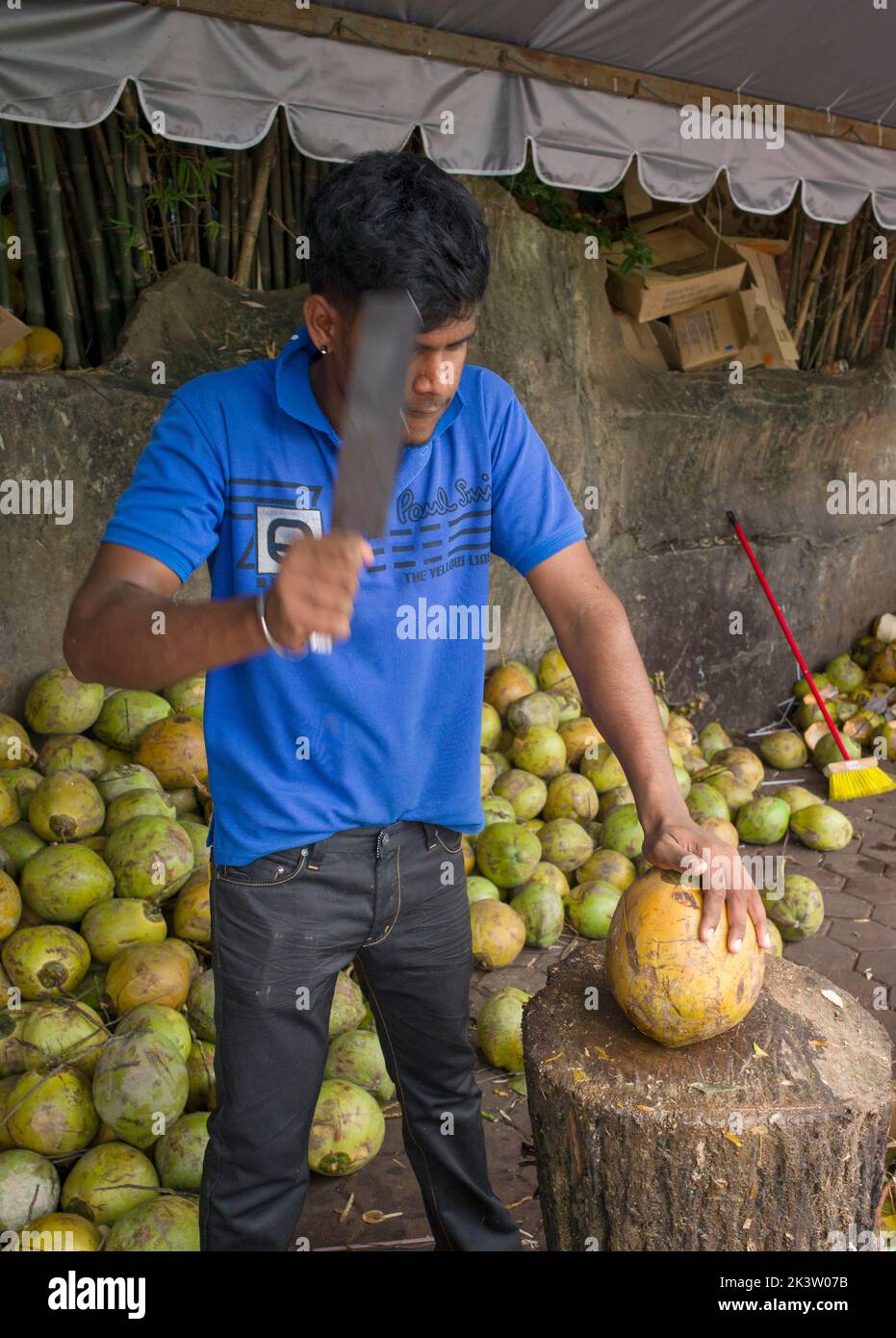 Young Malaysian man chops coconut for tourist refreshment on street