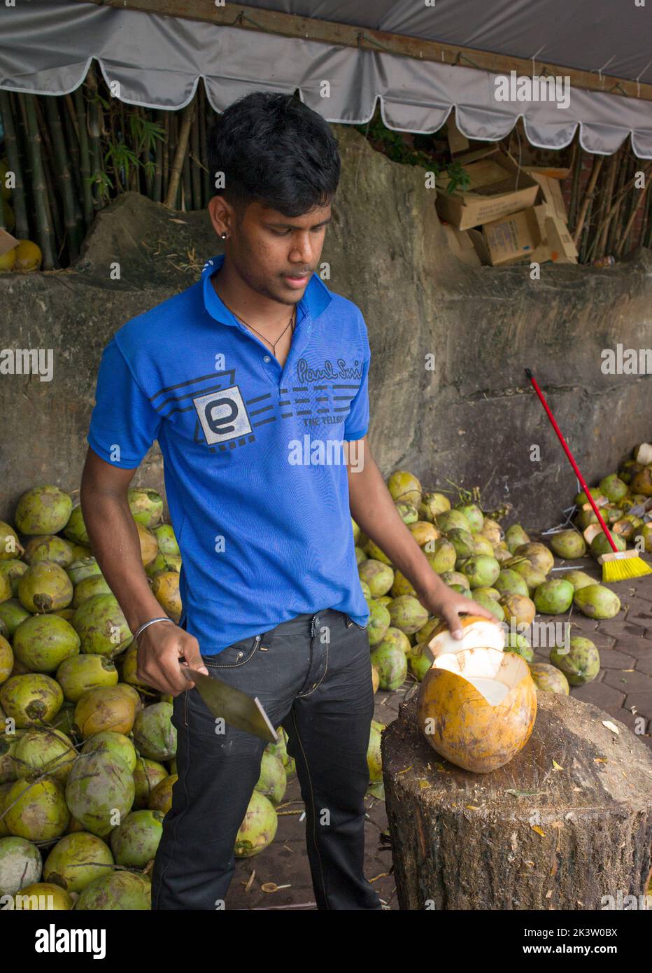 Young Malaysian man chops coconut for tourist refreshment on street