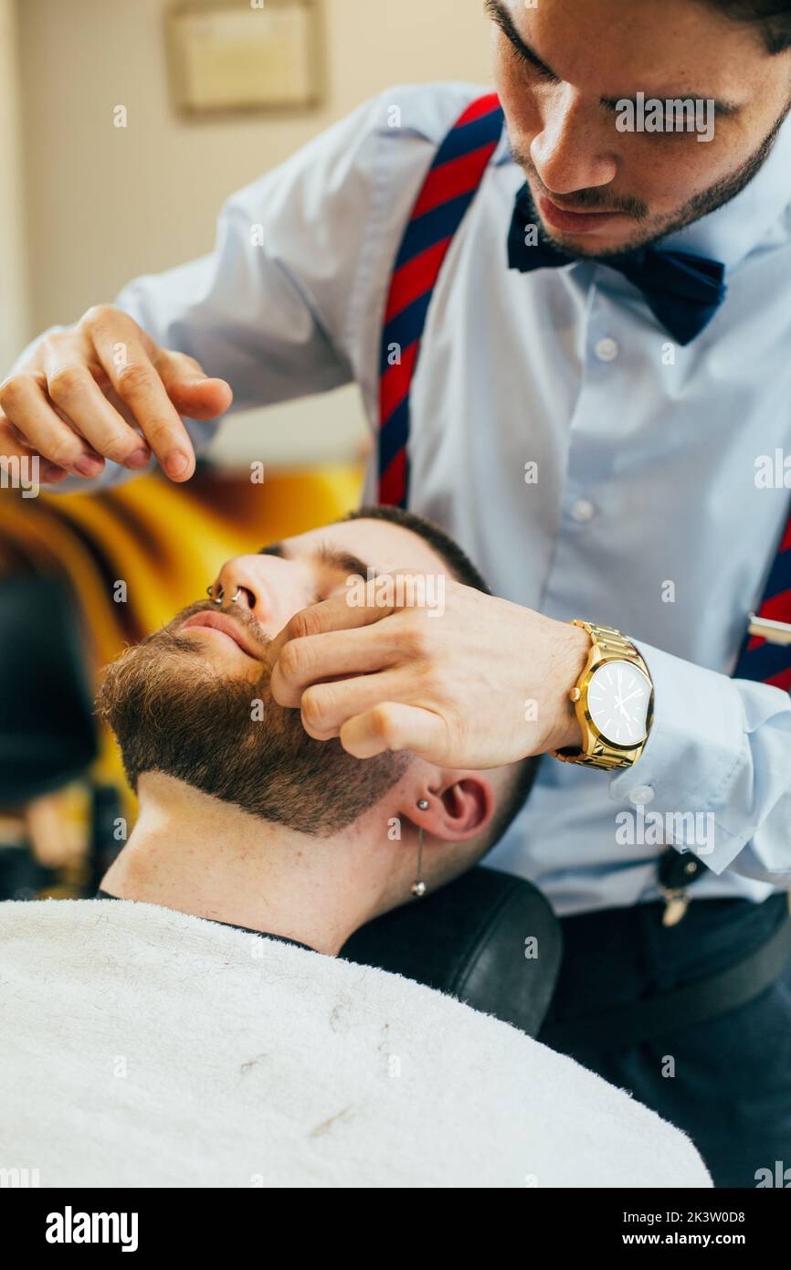 A barber cuts the beard of a man with a razor in a barbershop Stock ...