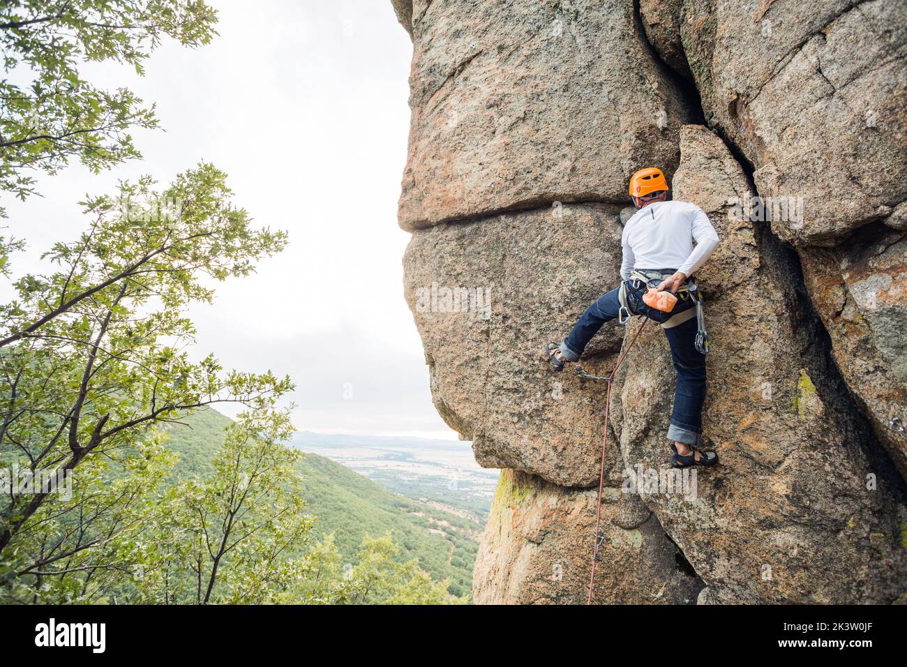 Male mountaineer climbing high cliff with safety carabiner and ropes
