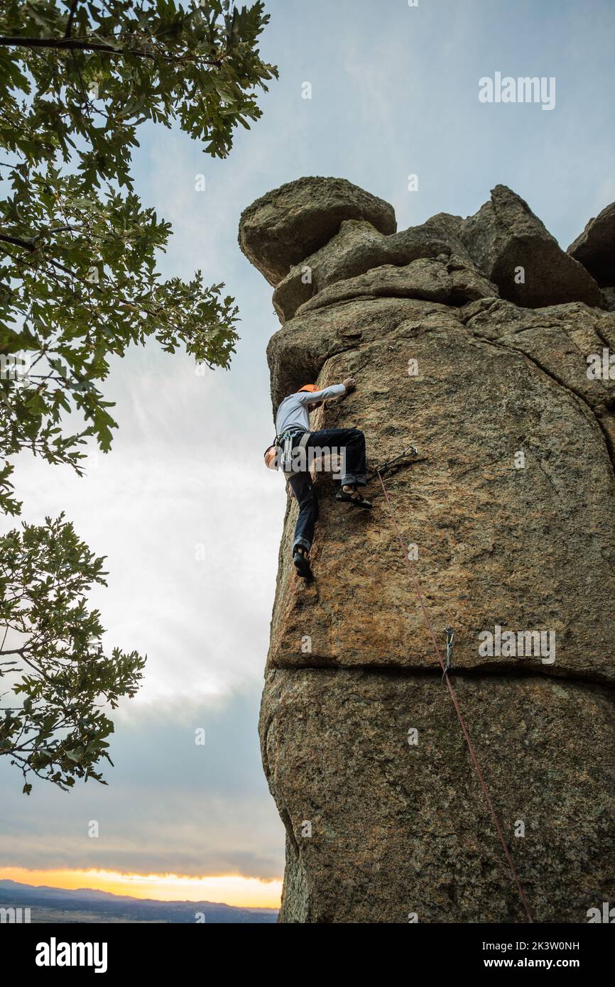 Male mountaineer climbing high cliff with safety carabiner and ropes
