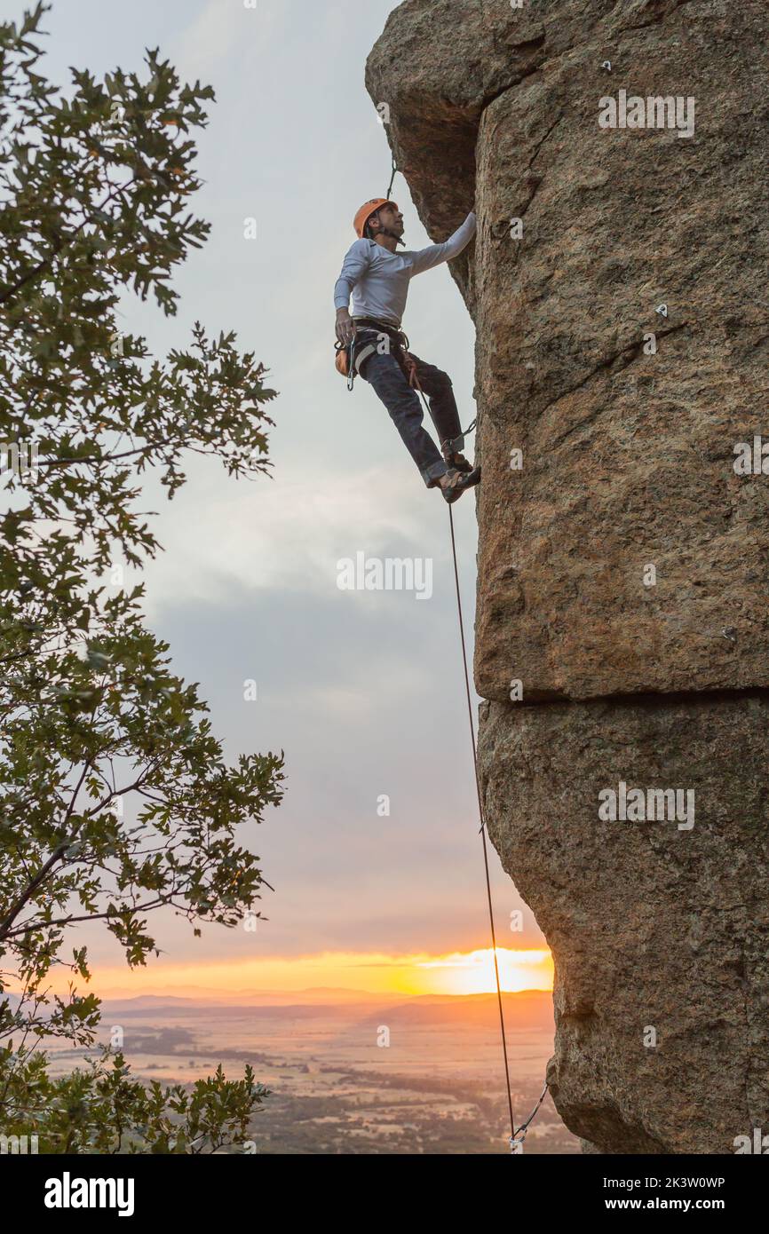 Male mountaineer climbing high cliff with safety carabiner and ropes