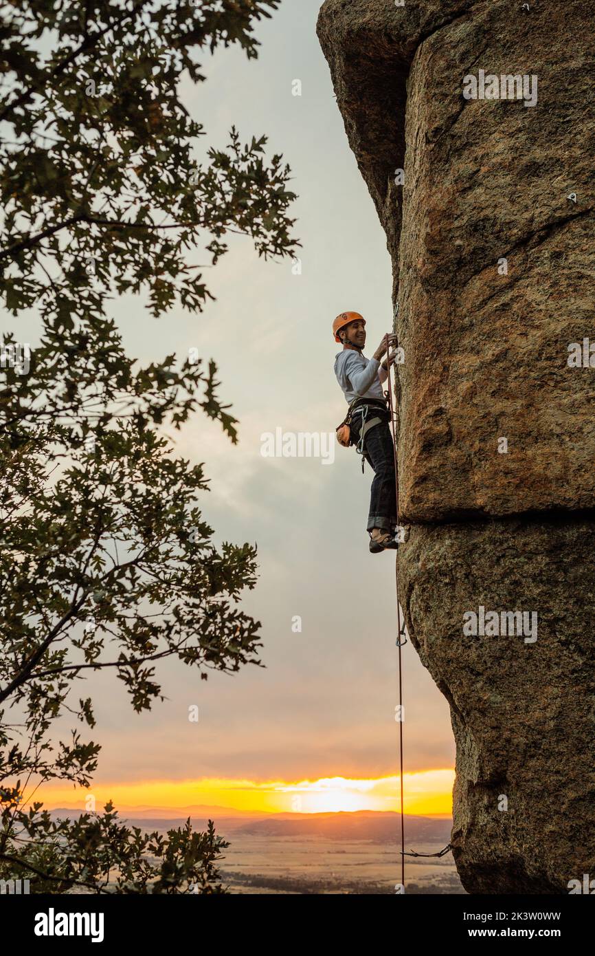 Male mountaineer climbing high cliff with safety carabiner and ropes ...