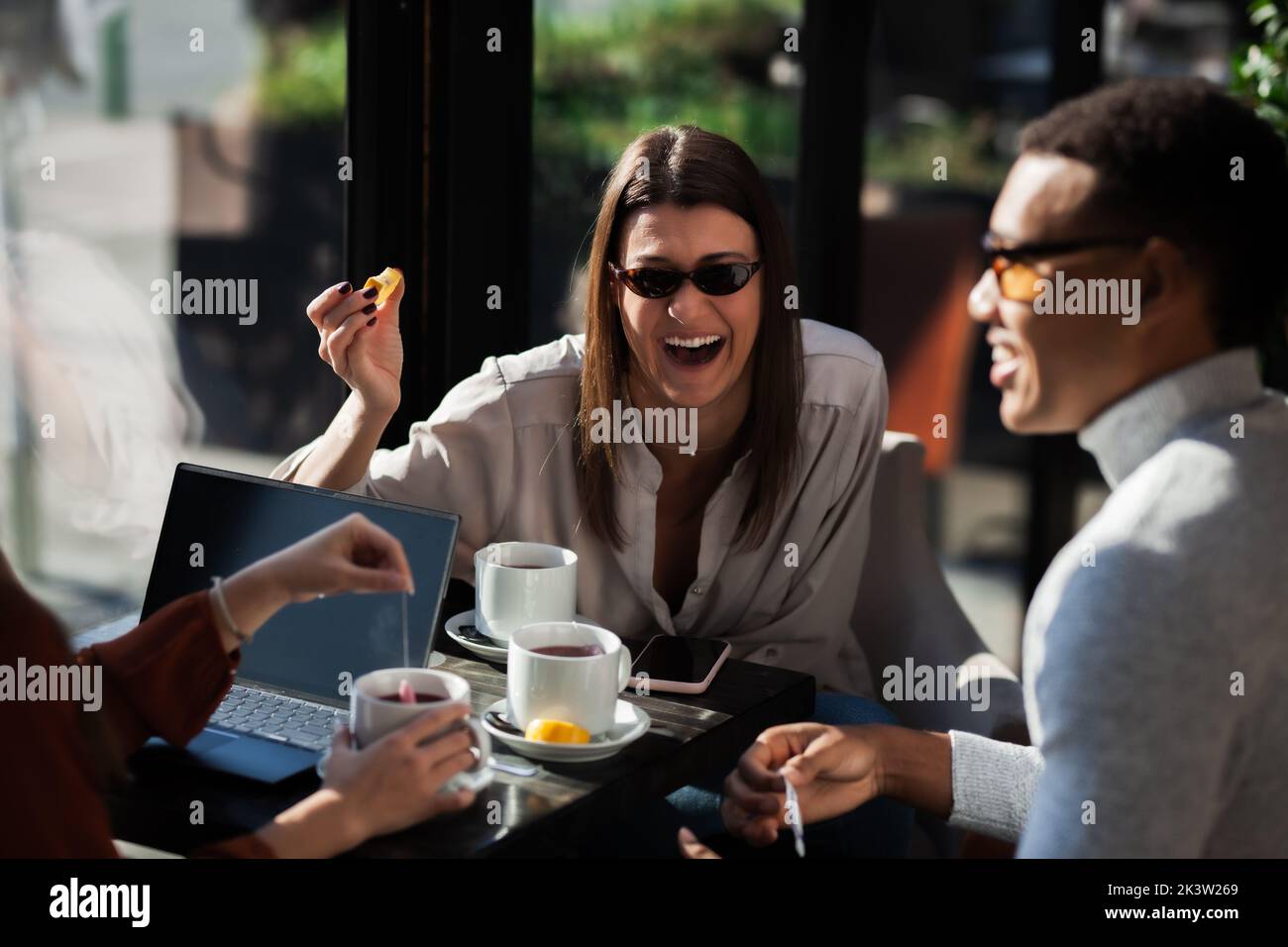 Three friends in a restaurant talking smiling and drinking tea. Business colleagues having a meeting after work or during coffee break at a cafe bar. Stock Photo