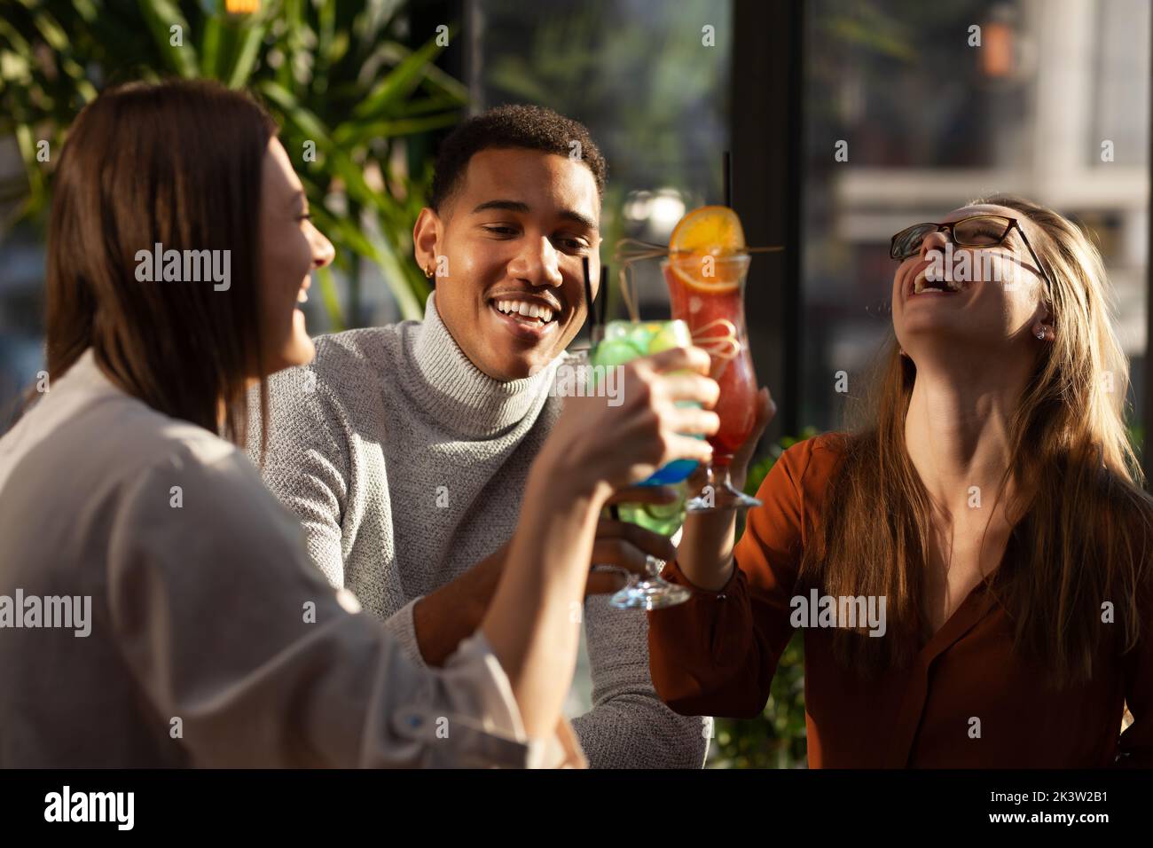 Three multiracial friends in a bar cheering. After work party with cocktails after successful work day. Stock Photo