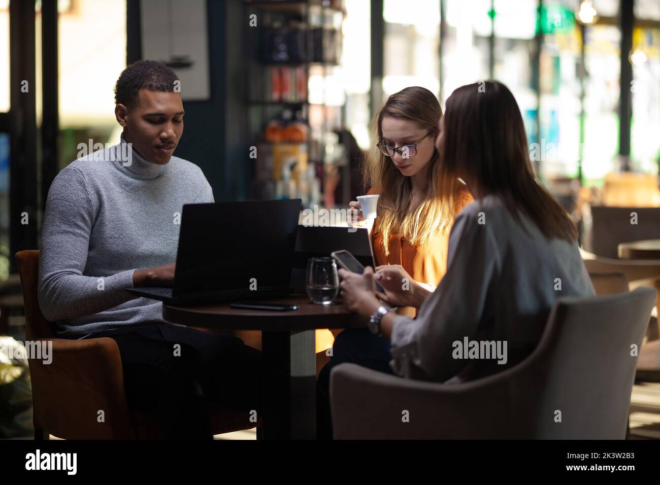 Three multiracial business colleagues having a meeting after work or during coffee break in a restaurant. Friends working at a cafe bar. Stock Photo