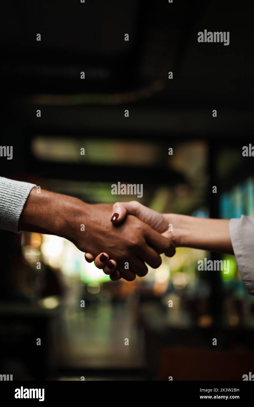 Two multiracial business colleagues working after work or during coffee break in a restaurant. Man and woman shaking hands after successful meeting. Stock Photo