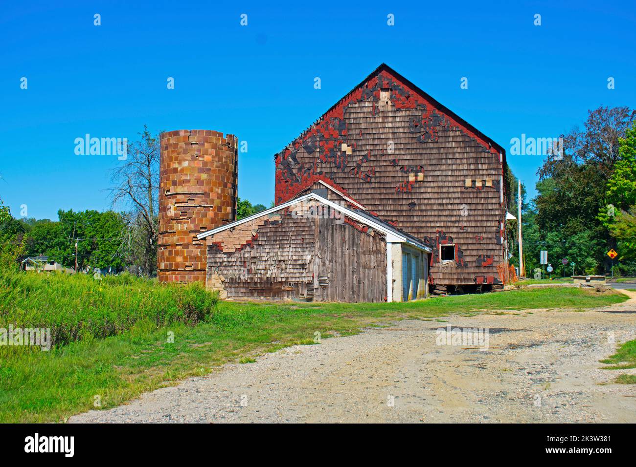 Old red barn in badly need of repairs, on a grassy field on a clear and sunny day -02 Stock Photo
